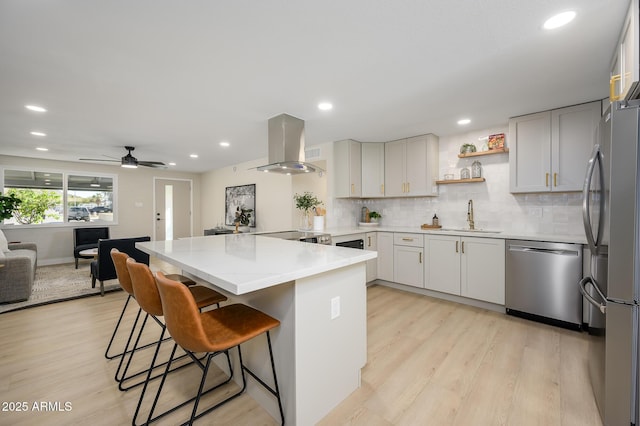 kitchen featuring sink, stainless steel appliances, island range hood, a kitchen bar, and kitchen peninsula