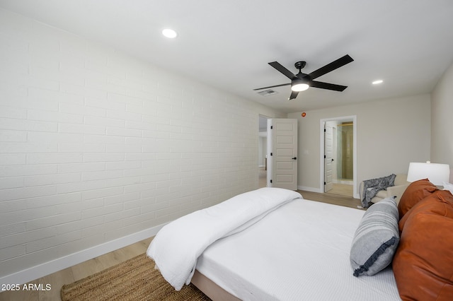 bedroom with connected bathroom, hardwood / wood-style floors, ceiling fan, and brick wall