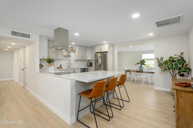 kitchen with island range hood, tasteful backsplash, a breakfast bar area, kitchen peninsula, and stainless steel refrigerator with ice dispenser