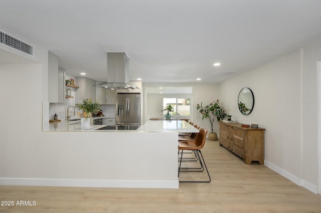 kitchen with sink, a breakfast bar area, island exhaust hood, kitchen peninsula, and stainless steel refrigerator with ice dispenser