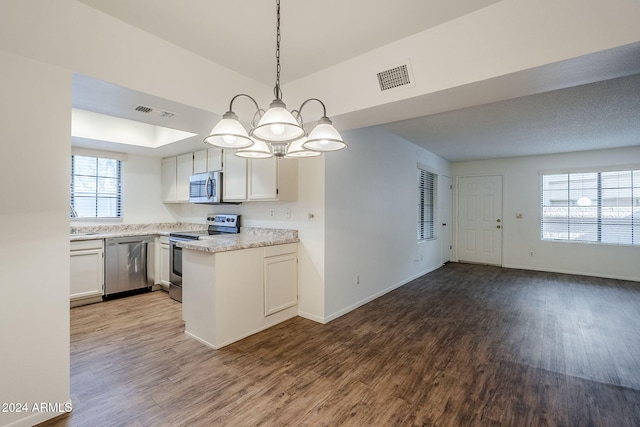 kitchen with white cabinets, stainless steel appliances, decorative light fixtures, and hardwood / wood-style flooring