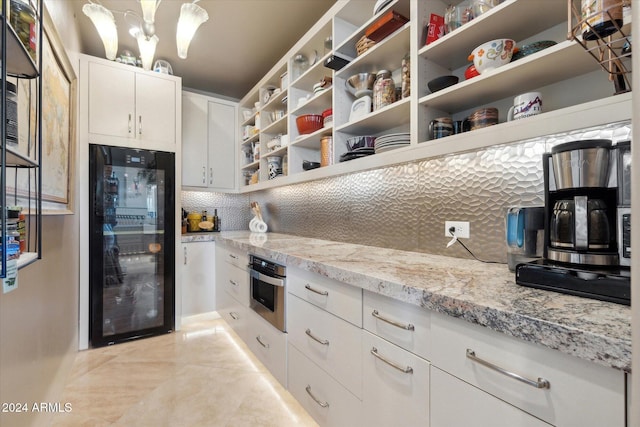 kitchen with light stone countertops, black refrigerator, stainless steel oven, pendant lighting, and white cabinets