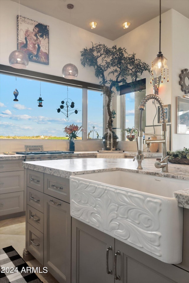 kitchen with gray cabinetry, light stone counters, sink, and pendant lighting