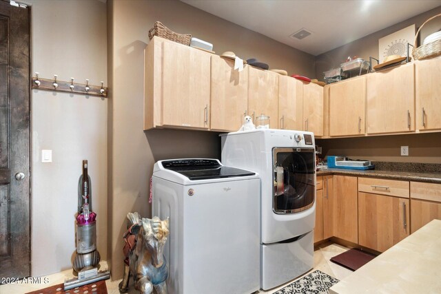 laundry area featuring washing machine and dryer, light tile patterned floors, and cabinets