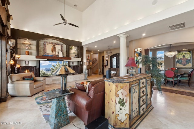 living room featuring ornate columns, built in shelves, a towering ceiling, and ceiling fan with notable chandelier