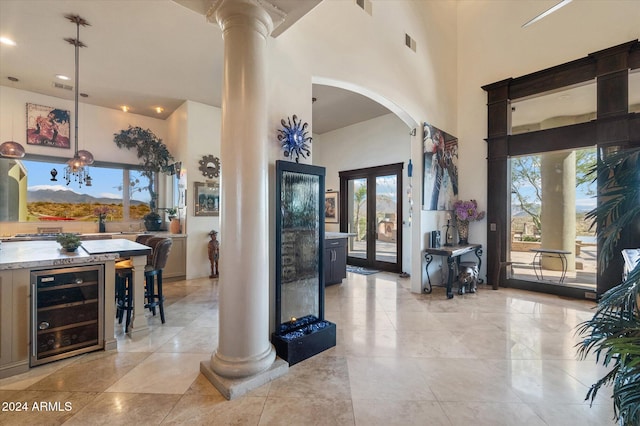 foyer featuring decorative columns, french doors, a towering ceiling, and beverage cooler