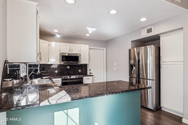 kitchen featuring stainless steel appliances, visible vents, decorative backsplash, a sink, and a peninsula