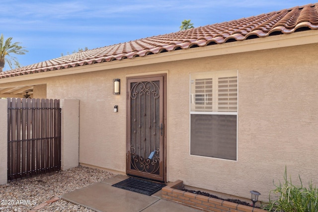 doorway to property with a tile roof, fence, and stucco siding