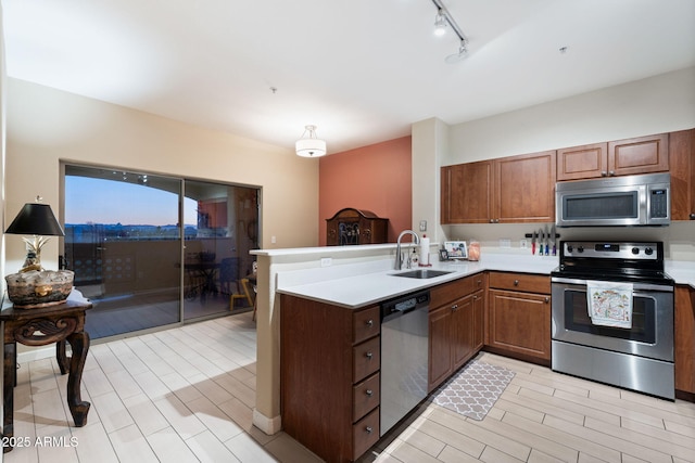 kitchen with track lighting, appliances with stainless steel finishes, kitchen peninsula, and sink