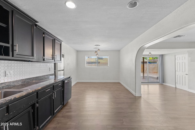 6714 N 26th Dr, Phoenix, AZ 85017 - kitchen with tasteful backsplash, light wood-type flooring, a textured ceiling, dark cabinetry, and arched walkways