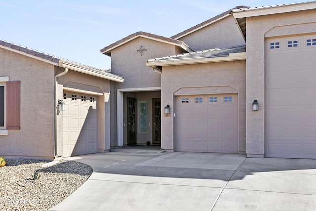 view of front of house featuring an attached garage, driveway, a tiled roof, and stucco siding