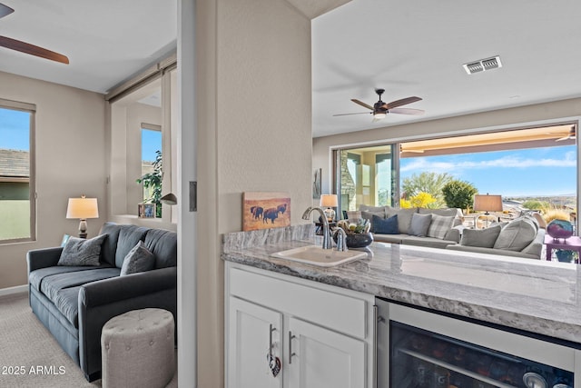 interior space featuring light stone countertops, a wealth of natural light, beverage cooler, sink, and white cabinetry