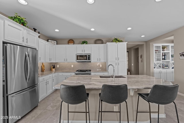 kitchen featuring light stone countertops, a kitchen bar, stainless steel appliances, white cabinetry, and an island with sink