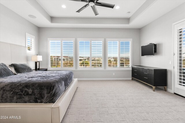 carpeted bedroom featuring ceiling fan, multiple windows, and a tray ceiling