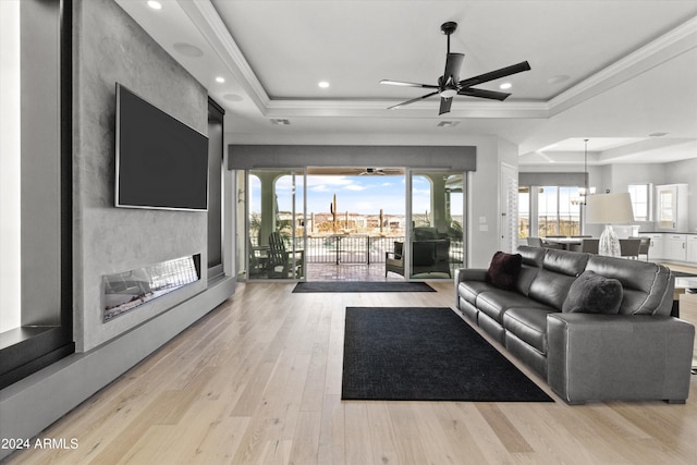 living room featuring light wood-type flooring, a tray ceiling, and ceiling fan with notable chandelier