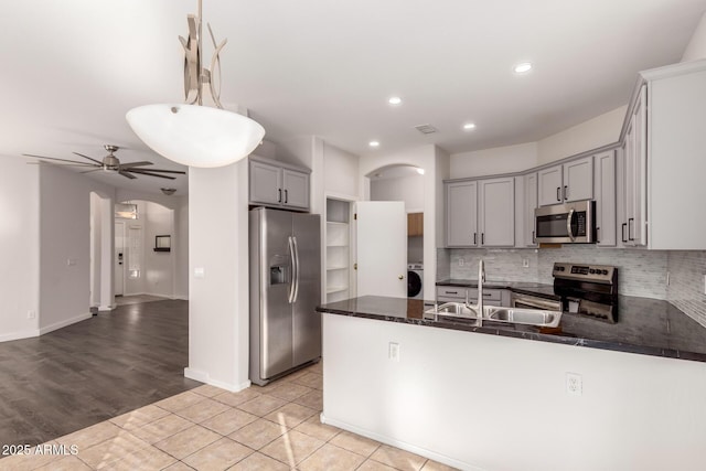 kitchen featuring washer / dryer, kitchen peninsula, appliances with stainless steel finishes, pendant lighting, and sink