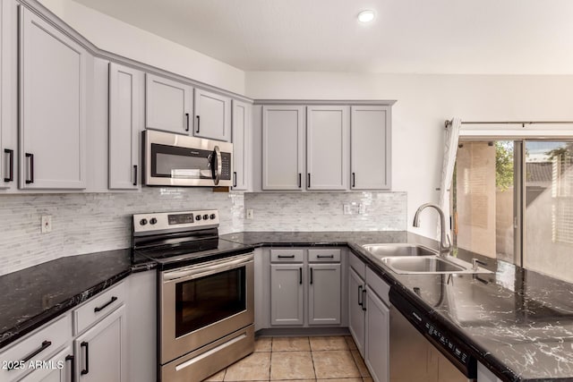 kitchen with light tile patterned floors, appliances with stainless steel finishes, gray cabinetry, dark stone counters, and sink