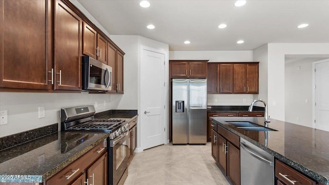 kitchen with dark stone countertops, a sink, light tile patterned floors, appliances with stainless steel finishes, and recessed lighting