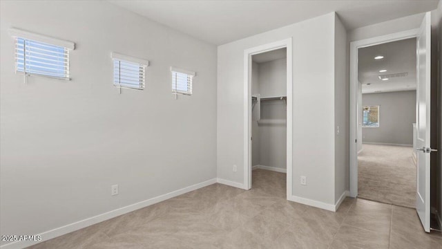 unfurnished bedroom featuring a walk in closet, light carpet, multiple windows, and baseboards