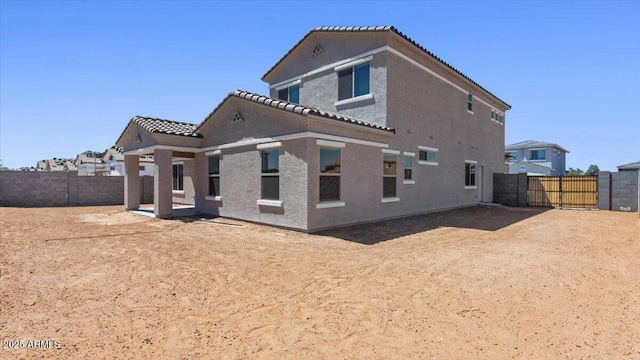 back of house featuring a gate, a tile roof, a fenced backyard, and stucco siding