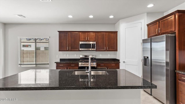 kitchen featuring dark stone counters, a sink, a center island with sink, appliances with stainless steel finishes, and recessed lighting