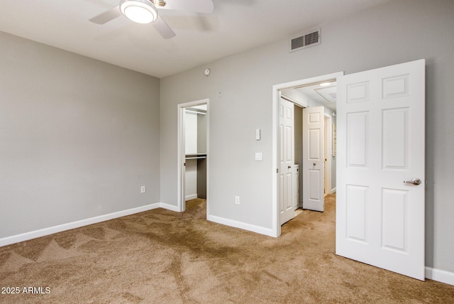 unfurnished bedroom featuring a walk in closet, light colored carpet, a closet, and ceiling fan
