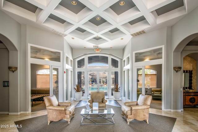 tiled living room with coffered ceiling, a towering ceiling, beam ceiling, and french doors