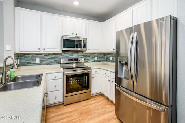 kitchen featuring appliances with stainless steel finishes, sink, white cabinets, decorative backsplash, and light wood-type flooring