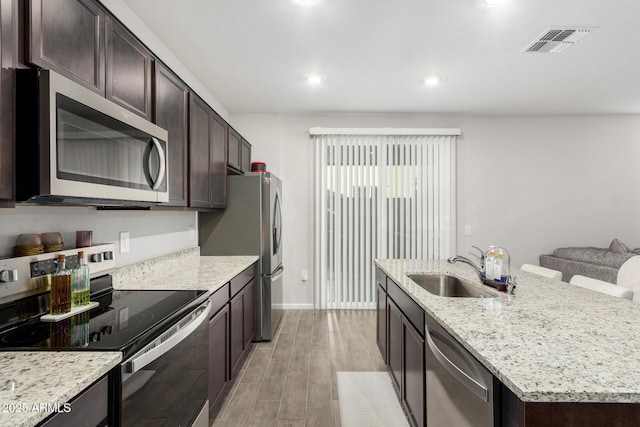 kitchen with sink, a center island with sink, light hardwood / wood-style flooring, appliances with stainless steel finishes, and light stone countertops