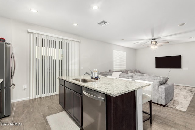 kitchen with sink, a center island with sink, stainless steel appliances, light stone countertops, and light hardwood / wood-style floors