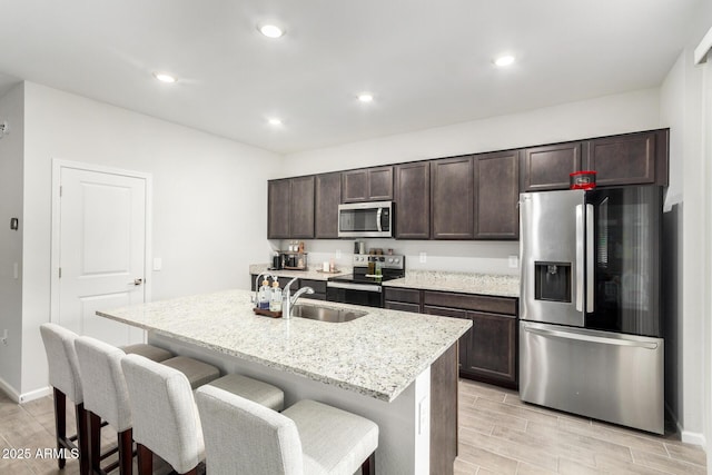 kitchen with sink, a breakfast bar area, appliances with stainless steel finishes, dark brown cabinetry, and an island with sink