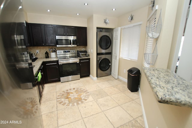 kitchen featuring stacked washer and dryer, light stone counters, stainless steel appliances, and tasteful backsplash