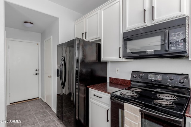 kitchen with dark stone counters, black appliances, light tile patterned flooring, and white cabinetry