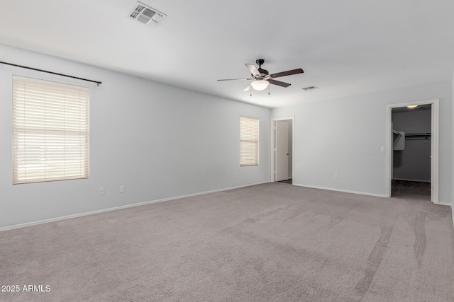 empty room with carpet flooring, a ceiling fan, visible vents, and a wealth of natural light