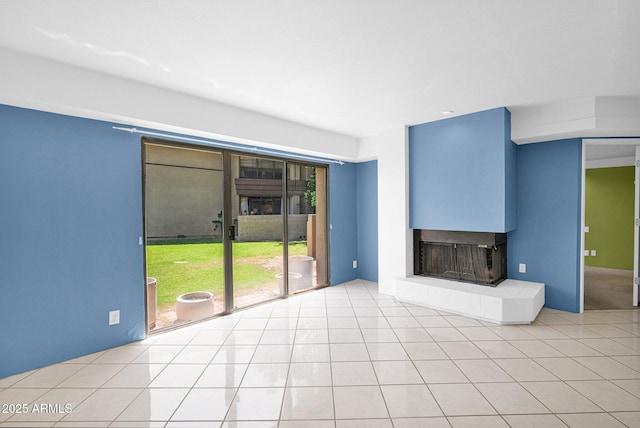 unfurnished living room featuring a multi sided fireplace and light tile patterned flooring