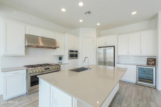 kitchen featuring sink, wine cooler, range hood, an island with sink, and high end appliances