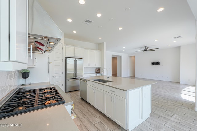 kitchen featuring a center island with sink, sink, range hood, appliances with stainless steel finishes, and white cabinetry