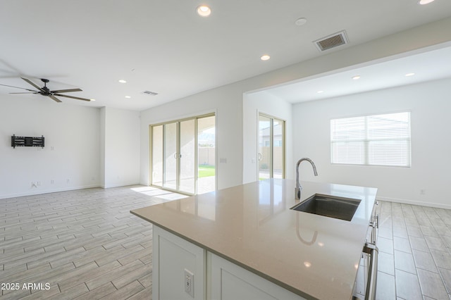 kitchen with stone counters, white cabinetry, sink, ceiling fan, and a center island with sink