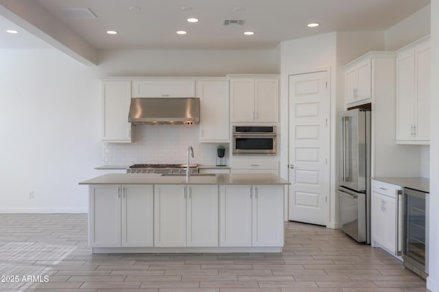 kitchen with a kitchen island with sink, ventilation hood, wine cooler, white cabinetry, and stainless steel appliances