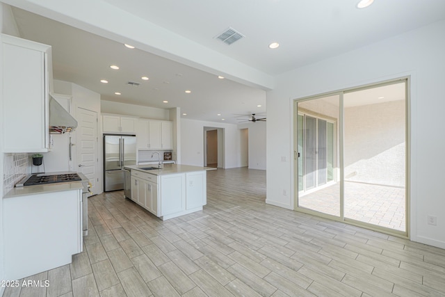 kitchen featuring white cabinets, stainless steel refrigerator, a kitchen island with sink, and ceiling fan