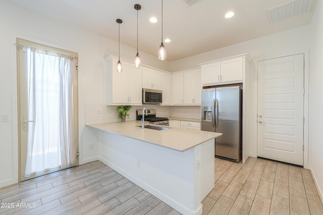 kitchen with kitchen peninsula, stainless steel appliances, sink, white cabinets, and hanging light fixtures