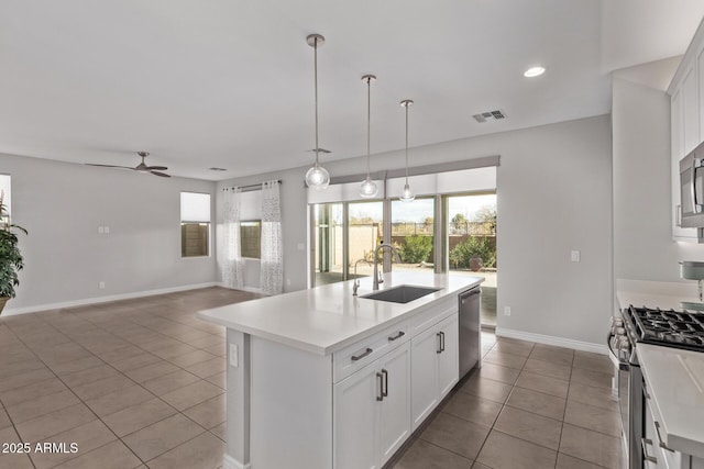 kitchen featuring pendant lighting, sink, appliances with stainless steel finishes, white cabinetry, and a center island with sink