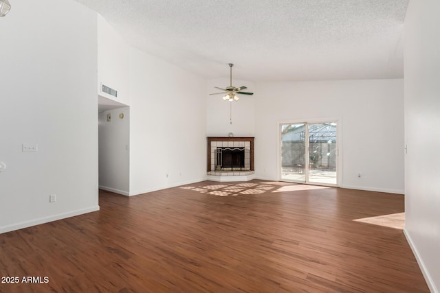 unfurnished living room with ceiling fan, dark hardwood / wood-style flooring, a tile fireplace, a textured ceiling, and high vaulted ceiling