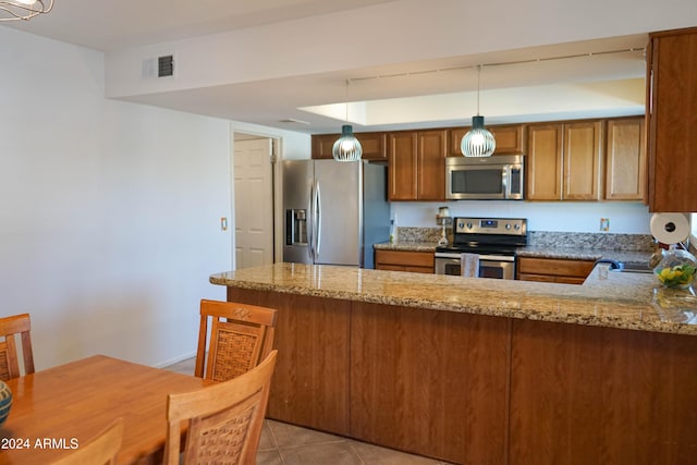 kitchen with light stone countertops, kitchen peninsula, hanging light fixtures, and appliances with stainless steel finishes