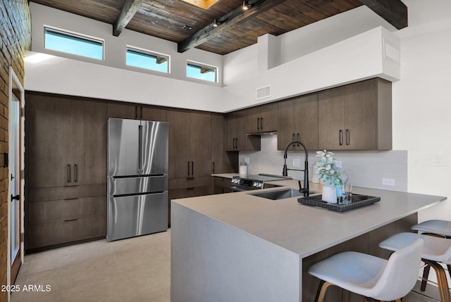 kitchen with stainless steel refrigerator, beamed ceiling, backsplash, a breakfast bar, and wood ceiling