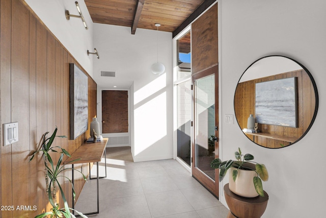 hallway featuring beamed ceiling, wood walls, wooden ceiling, and light tile patterned floors