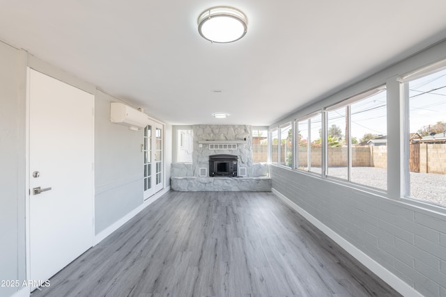 6316 N 23rd Ave, Phoenix, AZ 85015 - unfurnished living room with wood finished floors, baseboards, a wall mounted air conditioner, and a stone fireplace