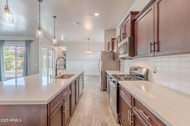 809 W Coles Rd, Phoenix, AZ 85041 - kitchen with appliances with stainless steel finishes, a sink, wainscoting, a center island with sink, and light wood-style flooring