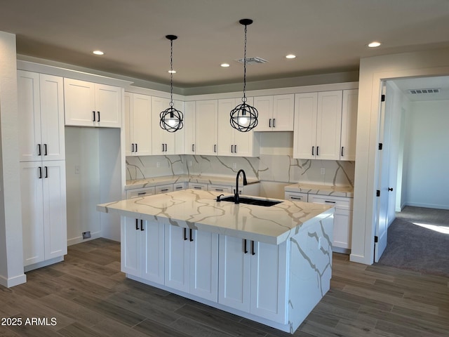 kitchen with sink, white cabinets, hanging light fixtures, a kitchen island with sink, and light stone countertops