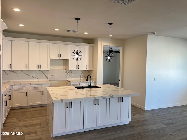 kitchen featuring sink, white cabinetry, light stone counters, an island with sink, and decorative light fixtures